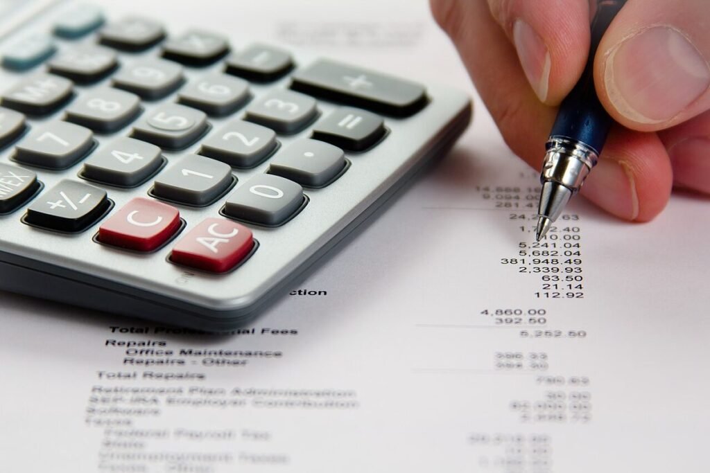 Calculatrice posée sur un relevé financier chiffré, une main tenant un stylo à côté