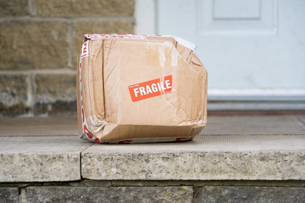 Carton marqué « Fragile » enfoncé et déchiré, déposé sur le seuil d'une porte